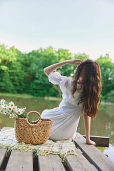 a woman with well-groomed hair is resting on the pier sitting with her back to the camera enjoying nature. High quality photo