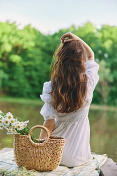 a woman with well-groomed hair is resting on the pier sitting with her back to the camera enjoying nature. High quality photo