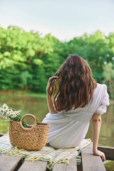 a woman with well-groomed hair is resting on the pier sitting with her back to the camera enjoying nature. High quality photo