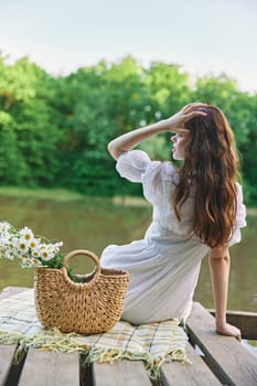 a woman with well-groomed hair is resting on the pier sitting with her back to the camera enjoying nature. High quality photo