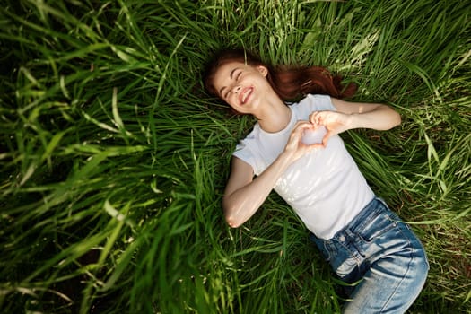 happy woman folded her arms on her chest in the shape of a heart lying in the grass. High quality photo
