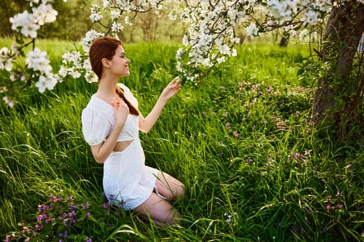 a woman in a light dress sits in the grass near a flowering apple tree. High quality photo