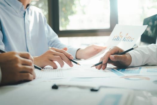 Close-up of businessmen working together at workplace, discussing about strategies, plans, analytic progress, and financial stats, and pointing at graph documents on desk holding pencils. Business and Teamwork concept.