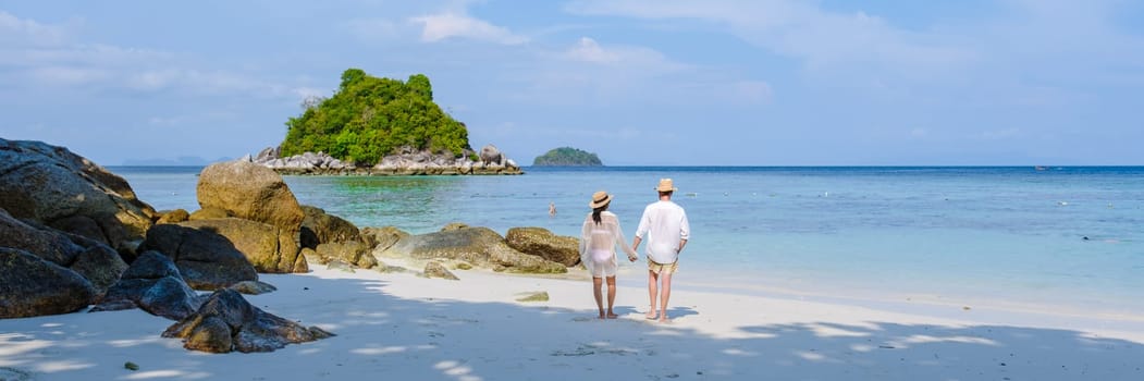Koh Lipe Island Southern Thailand with turqouse colored ocean and white sandy beach at Ko Lipe. a couple of men and women on vacation in Thailand walking at the beach