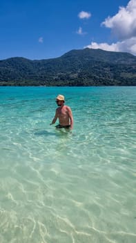 Young men in swim short at the beach of Koh Lipe Island Southern Thailand with turqouse colored ocean and white sandy beach at Ko Lipe.