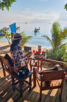 woman having breakfast with coffee at the beach of Koh Lipe Island Southern Thailand with turqouse colored ocean and white sandy beach at Ko Lipe.