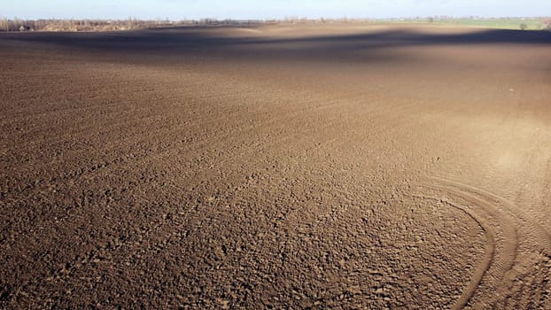 Landscape of plowed up land on agricultural field with cloud shadows on sunny autumn day. Flying over plowed earth with black soil. Agrarian background. Ground earth dirt priming. Aerial drone view.