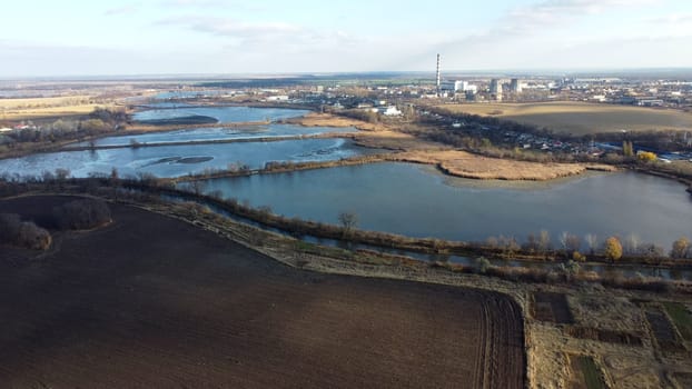 Urban beautiful landscape agricultural plowed fields, lakes for growing fish, gardens, thermal power plant, building industrial area of city, cloud shadows on sunny autumn day. Aerial drone view.