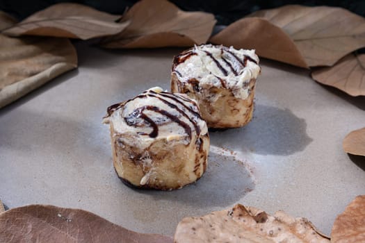 Two Soft Chocolate Buns topped with rich cream cheese frosting on ceramic tray with dark background. The concept of delicious food, Space for text, Selective Focus.