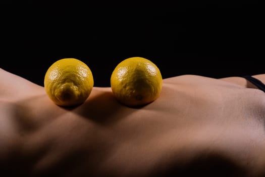 Young woman with cellulite problem and lemon on a dark background, closeup