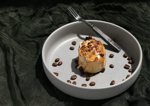 Caramel Pecanbon topped with decadent caramel frosting and pecans served with Coffee beans and Metal fork on ceramic plate with dark background. Space for text, Selective focus.