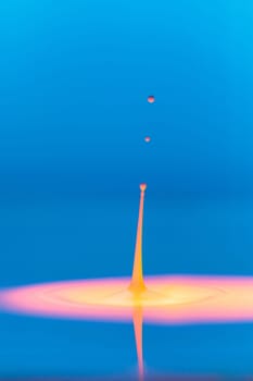 A drop falls into a thick liquid with a blue-yellow background. Abstract colorful background