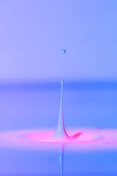 A drop falls into a thick liquid with a blue-pink background. Abstract colorful background