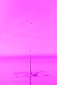 A drop falls into a thick liquid with a pink background. Abstract colorful background