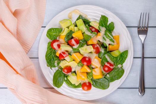 Fresh salad of avocado, mango, spinach and cherry tomatoes in a white plate on a wooden background. High quality photo