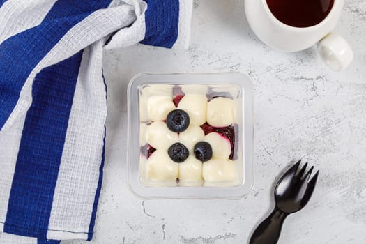 Dessert of cream, jam and blueberries in a plastic glass on a concrete background. High quality photo