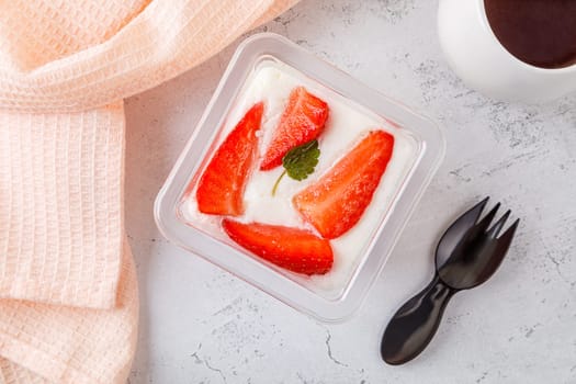 Dessert of white and pink cream with strawberries in a plastic container on a concrete background. High quality photo