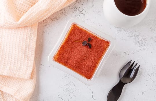Tiramisu dessert in a plastic box with a fork on a concrete background. High quality photo