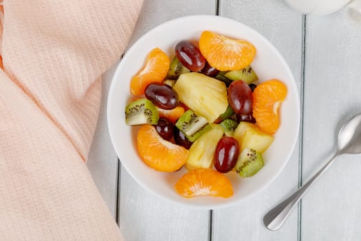 Fruit salad of pineapple, orange, kiwi and grapes in a plate on a wooden background. High quality photo