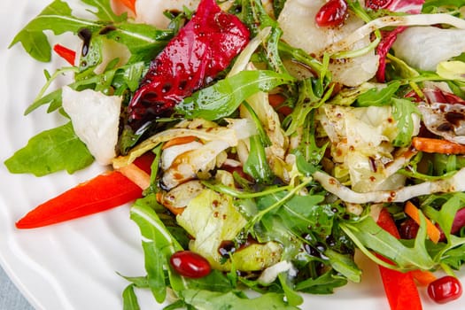 Fresh salad of cabbage, herbs, peppers, carrots and pomegranate seeds in a white plate. High quality photo