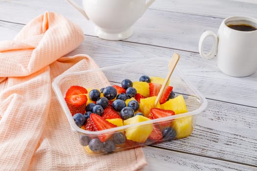 Fruit salad with pineapple, strawberries and blueberries in a plastic container on a wooden background. High quality photo