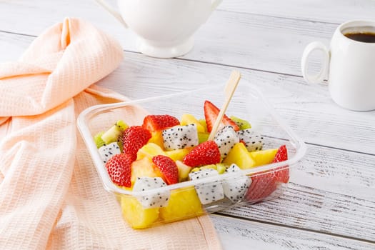 Fruit salad of pineapple, strawberries, kiwi and pitahaya in a plastic container on a wooden background. High quality photo
