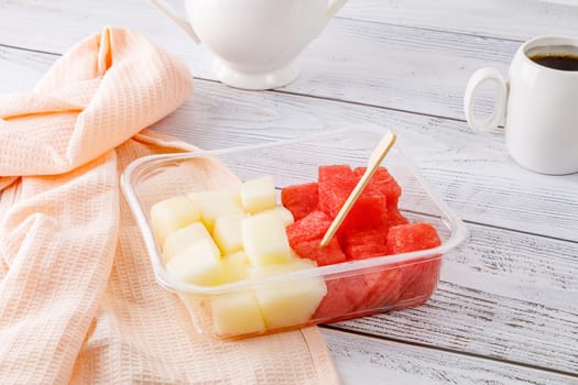 Fruit salad with watermelon and melon in a plastic container on a wooden background. High quality photo