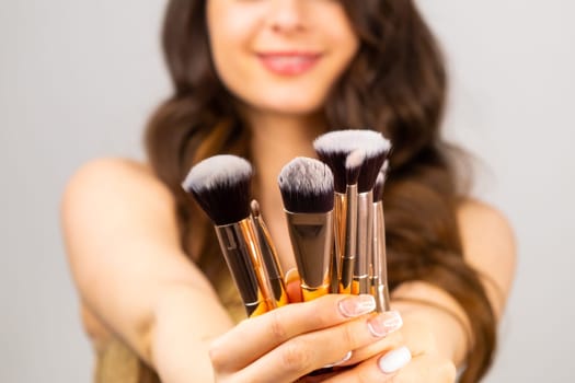 Professional makeup brushes in woman hands on the grey background.