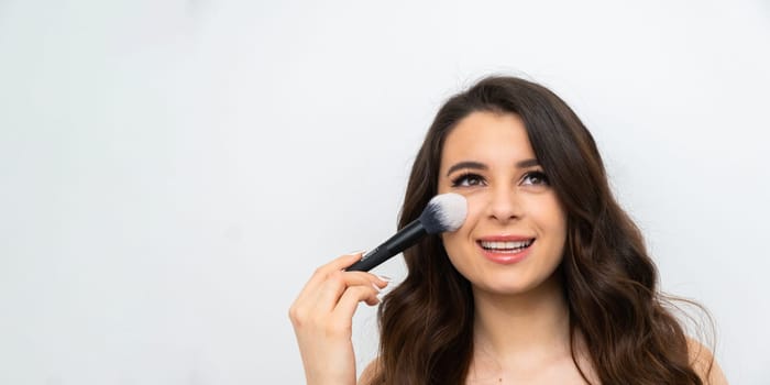Facial makeup. Young smiling woman applying blush with a cosmetic brush. Beauty concept on the banner with copy space.