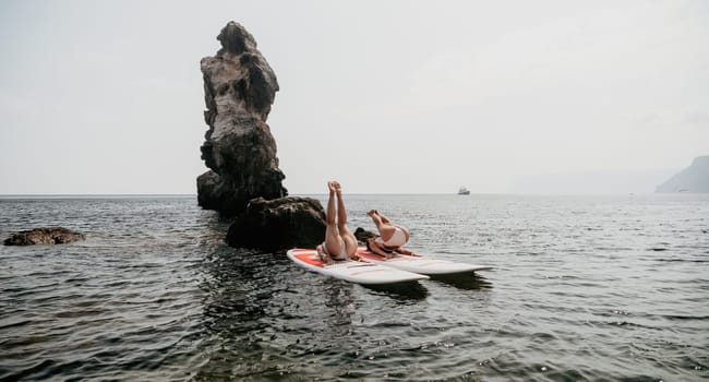 Woman sup yoga. Middle age sporty woman practising yoga pilates on paddle sup surfboard. Female stretching doing workout on sea water. Modern individual hipster outdoor summer sport activity