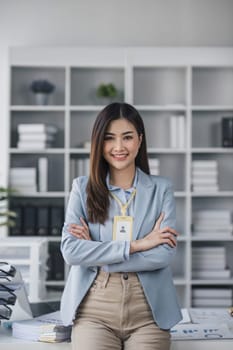 Attractive asian businesswoman standing with crossed arms and looking at camera in office confident and happy with business success..