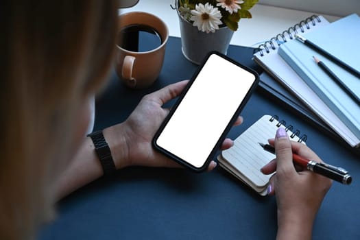 Young woman holding smart phone and making notes on notebook. Blank screen for advertise text.
