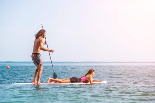 Silhouette of woman standing, surfing on SUP board, confident paddling through water surface. Idyllic sunset or sunrise. Sports active lifestyle at sea or river.