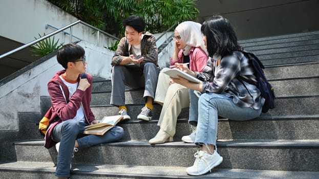 Group of university students sitting on stairs and talking to each other after classes. Education and youth lifestyle concept.