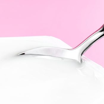 Yogurt cup and silver spoon on pink background, white plastic container with yoghurt cream, fresh dairy product for healthy diet and nutrition balance.