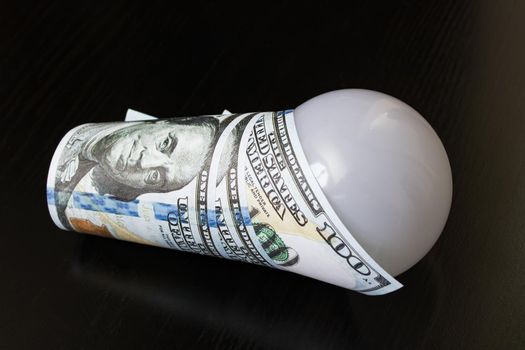 Light bulb wrapped in dollars on a wooden table