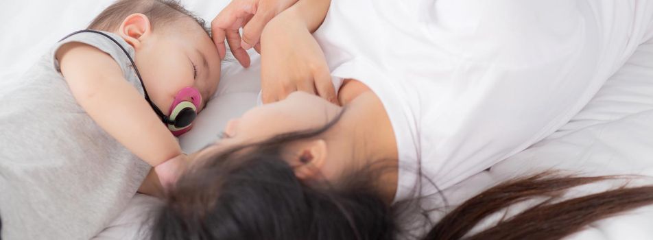 Young asian mother touch head of little baby girl with tender on bed in the bedroom, mom love newborn and care, woman with expression with child together, parent and daughter, family concept.