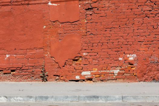 old brick wall with peeled off plaster, all over painted orange - background with sidewalk under it