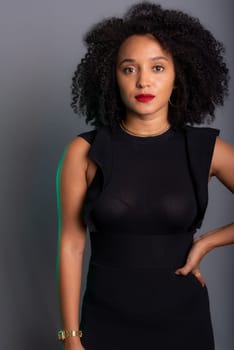 Beautiful young woman standing, serious, against gray background looking at the camera. studio portrait