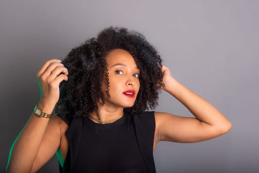 Portrait of beautiful young brunette woman messing with her hair. Dressed in black. Isolated on gray background