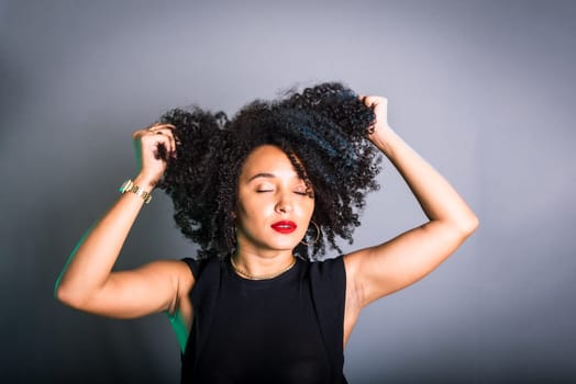 Portrait of beautiful young brunette woman messing with her hair. Dressed in black. Isolated on gray background