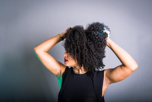 Portrait of beautiful young brunette woman messing with her hair. Dressed in black. Isolated on gray background