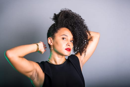 Portrait of beautiful young brunette woman messing with her hair. Dressed in black. Isolated on gray background