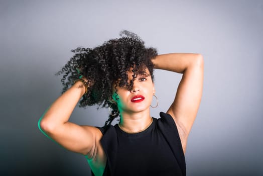 Beautiful young woman standing against gray background messing with her black hair. studio portrait