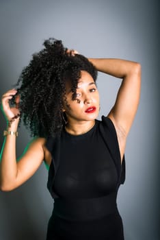 Beautiful young woman standing against gray background messing with her black hair. studio portrait