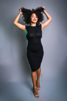 Beautiful young woman standing against gray background messing with her black hair. studio portrait