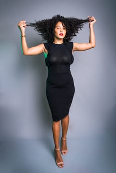 Beautiful young woman standing against gray background messing with her black hair. studio portrait