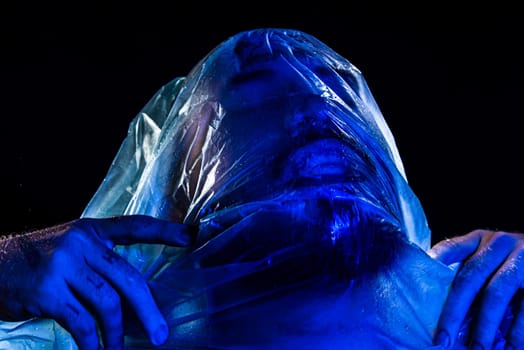 Man with plastic bag over his head, suffocated. Studio shot with blue filter. Isolated on black background.