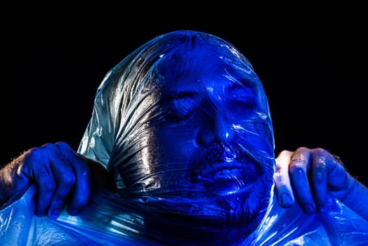 Man with plastic bag over his head, suffocated. Studio shot with blue filter. Isolated on black background.