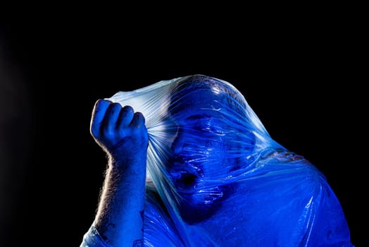 Man with plastic bag over his head, suffocated. Studio shot with blue filter. Isolated on black background.